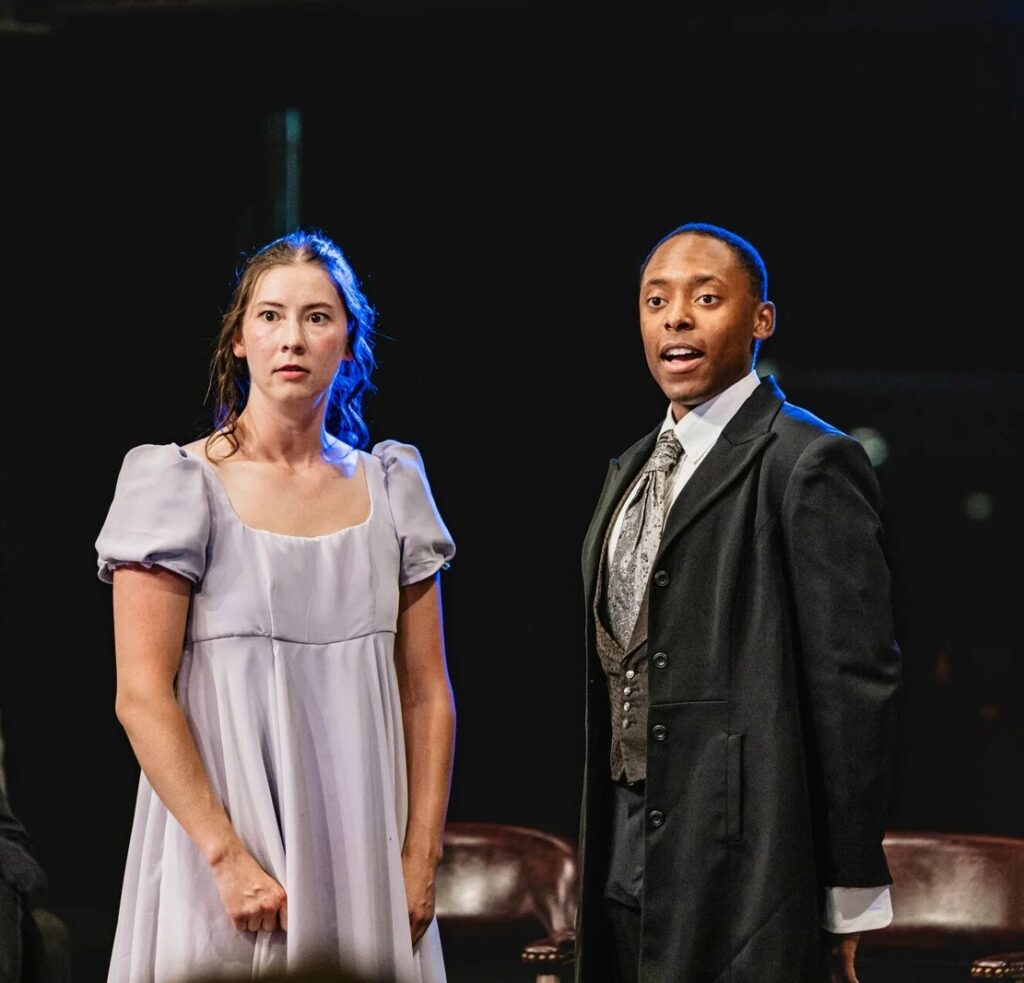 A woman in a period dress and a man in a suit perform Pride and Prejudice